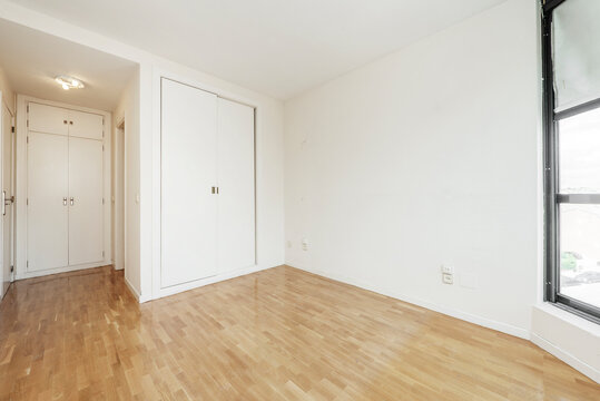 Built-in wardrobes with sliding wooden doors in an empty room with oak wooden floors