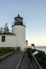 Fototapeta na wymiar The back of the Bass Head Harbor Lighthouse at sunset with bells at the end of the path