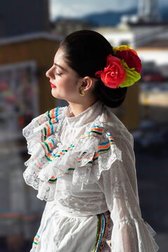 Portrait of Colombian young lady with sunlight on face and window in the background, with flowers in hair dressed in traditional Tolima folklore dress