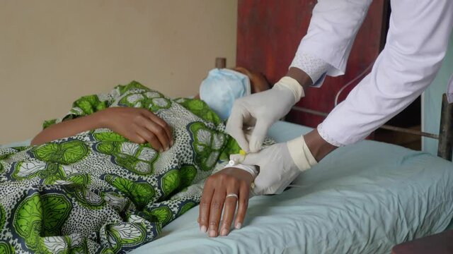 Close up shot of an African doctor putting and IV drip into an African woman's hand in a rural clinc.