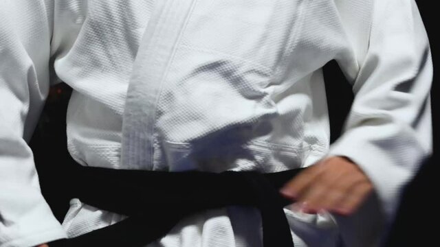 Close up of young man tying black belt around a white uniform, gi, martial arts fitness concept, accomplishing a goal
