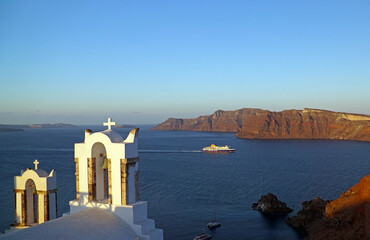 greek orthodox church bells in oia as ship passes by in the ocean background