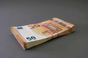 Stack of 50 euro banknotes, tied with rubber band, on a gray-blue background. Euro money. Close up view.