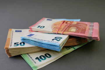 Stacks of 10, 20, 50 and 100 euro banknotes, tied with rubber band and lying one on one, isolated on a grey background. Euro money. Close up view.
