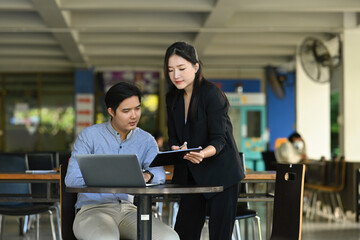 Photo of young businessman and businesswoman focussing on a clipboard at the working desk.
