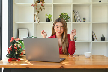 Photo of an attractive businesswoman using a computer laptop at the wooden table decorated by Christmas tree and over the bookshelf as a background.