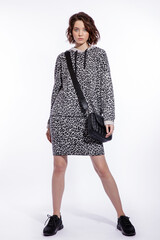 High fashion photo of a beautiful elegant young woman in a pretty gray leopard print blouse, skirt, black sneakers, handbag posing over white background. walking style. Make up, hairstyle. Slim figure
