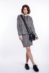 High fashion photo of a beautiful elegant young woman in a pretty gray leopard print blouse, skirt, black sneakers, handbag posing over white background. walking style. Make up, hairstyle. Slim figure