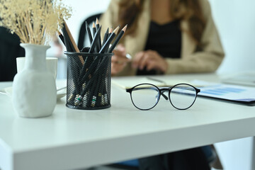 Photo of a comfortable workplace surrounded by eyeglasses, pencil holder and office accessories.