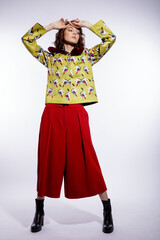 High fashion photo of a beautiful elegant young woman in a pretty yellow jacket with pattern flowers, red trousers, pants posing over white background. Make up, hairstyle. Slim figure. Studio shot