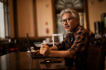 Businessman working on laptop in cafe. Handsome senior man enjoying in fresh coffee..
