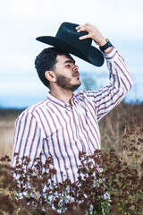 JOVEN MEXICANO CANTANDO CON SU GUITARRA USA SOMBRERO Y TIENE BARBA