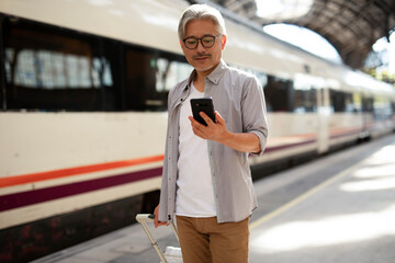Happy senior man waiting a train. Man using the phone while waiting a train.