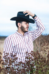 JOVEN MEXICANO CANTANDO CON SU GUITARRA USA SOMBRERO Y TIENE BARBA