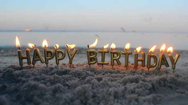 Candles Gold Letters Happy Birthday Burning on Background of Blurry Sea Waves on Sandy Beach. Burning Candles for Cake on Seaside. Concept Festive, Celebrating, Party, Birthday, Birthday Celebration
