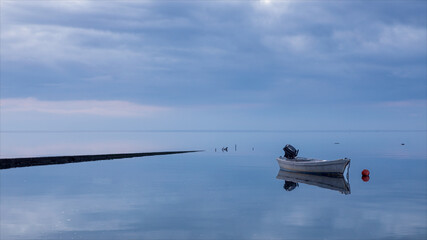 Motoscafo fermo ormeggiato in riva al mare all'alba. Cielo coperto da nuvole con i primi raggi di sole.