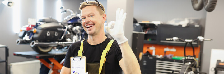 Happy male auto mechanic makes ok gesture in car service