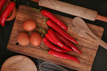 A few cayenne paper (Capsicum annuum), eggs, and cooking utensils on a wooden background.