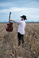 JOVEN MEXICANO CANTANDO CON SU GUITARRA USA SOMBRERO Y TIENE BARBA