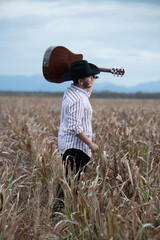 JOVEN MEXICANO CANTANDO CON SU GUITARRA USA SOMBRERO Y TIENE BARBA