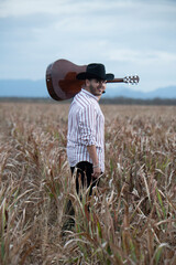 JOVEN MEXICANO CANTANDO CON SU GUITARRA USA SOMBRERO Y TIENE BARBA