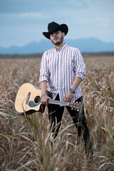 JOVEN MEXICANO CANTANDO CON SU GUITARRA USA SOMBRERO Y TIENE BARBA