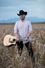 JOVEN MEXICANO CANTANDO CON SU GUITARRA USA SOMBRERO Y TIENE BARBA