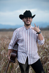 JOVEN MEXICANO CANTANDO CON SU GUITARRA USA SOMBRERO Y TIENE BARBA