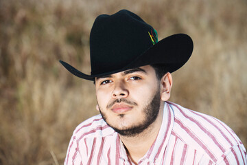 JOVEN MEXICANO CANTANDO CON SU GUITARRA USA SOMBRERO Y TIENE BARBA