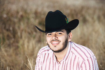 JOVEN MEXICANO CANTANDO CON SU GUITARRA USA SOMBRERO Y TIENE BARBA