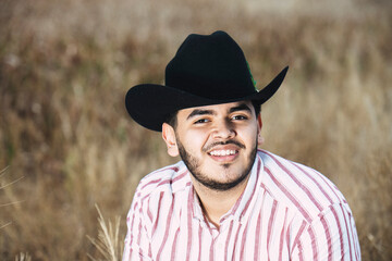 JOVEN MEXICANO CANTANDO CON SU GUITARRA USA SOMBRERO Y TIENE BARBA