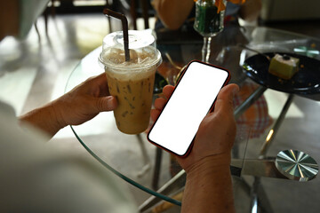 Photo of a man with medical mask holding an iced coffee and using a white blank screen smartphone at the glass table.