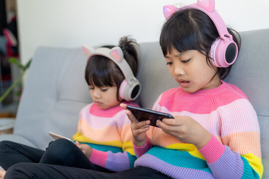 Asian siblings girl surfing net social media and playing on smartphone and digital tablet, e-learning at home
