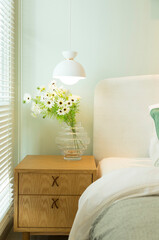 Green glass vase with bouquet of beautiful puppy flowers with lamp on side table in bedroom.