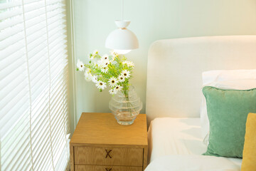 Green glass vase with bouquet of beautiful puppy flowers with lamp on side table in bedroom.