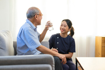 Smiling nurse giving glass of water to senior asian man in nursing home or assisted living facility.