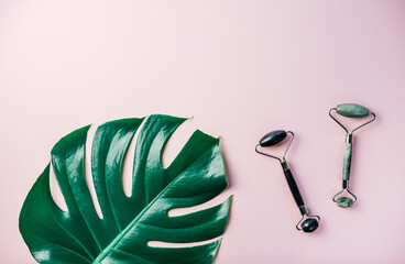 Gua sha facial massage rollers and tropical monstera leaf on pink background