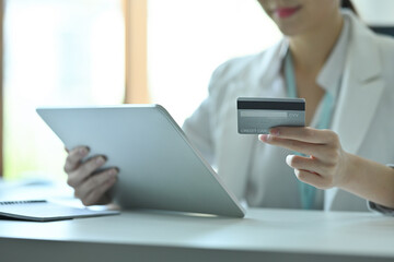Photo of a confident businesswoman holding a credit card and digital tablet at the modern working desk.