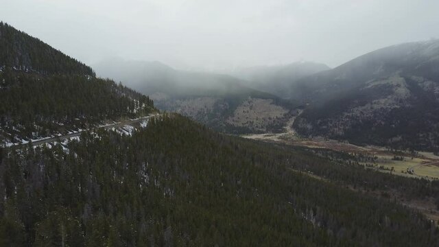 Snow falls on foggy mountains with a road on the side of the mountain