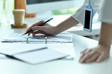 Cropped image of a young office woman standing and leaning on a working desk while writing on a paperwork.