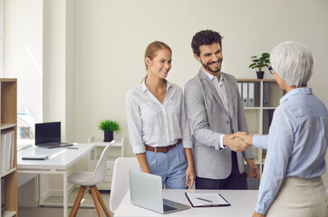 Happy married couple shaking hands with a female lawyer, realtor or financial advisor. Man and woman at a reception at an insurance broker or bank employee. Concept of business ethics and trust.