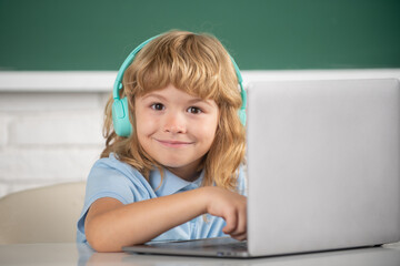 Smart funny boy in headphones sit at desk, study online on laptop at school, klever kid wear earphones in notebook learning using internet lessons. Genius child programming.