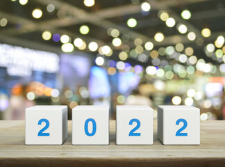 2022 letter on white block cubes on wooden table over blur light and shadow of shopping mall, Happy...
