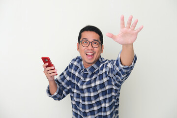 Adult Asian man holding mobile phone showing excited expression when trying to grab something that...