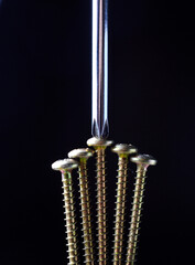 yellow self-tapping screw and chrome screwdriver on a dark background close-up.