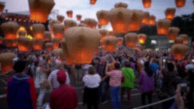 Blurred defocused view of people launching many asian fire lanterns during buddhist festival in chinese new year. Rice paper hot air balloons floating in traditional flying sky lantern