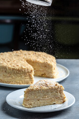 Napoleon Cake on a white plate. Traditional French dessert. chef hands with powder in a freeze motion of a cloud of powder midair