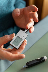 A close-up of an elderly person measures blood sugar with a glucometer. Blood on the test shelf to measure sugar. Lancet device on table.