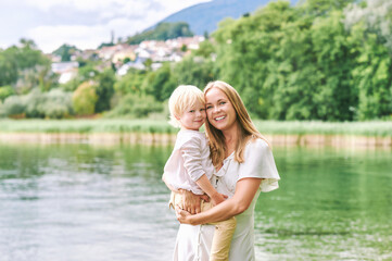 Fototapeta na wymiar Outdoor portrait of happy young mother with adorable preschooler son, enjoying nice day next to lake