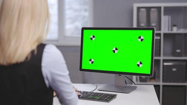 Middle aged business woman in formal wear sitting at office table and using modern pc with chroma key monitor. Back view, copy space.
